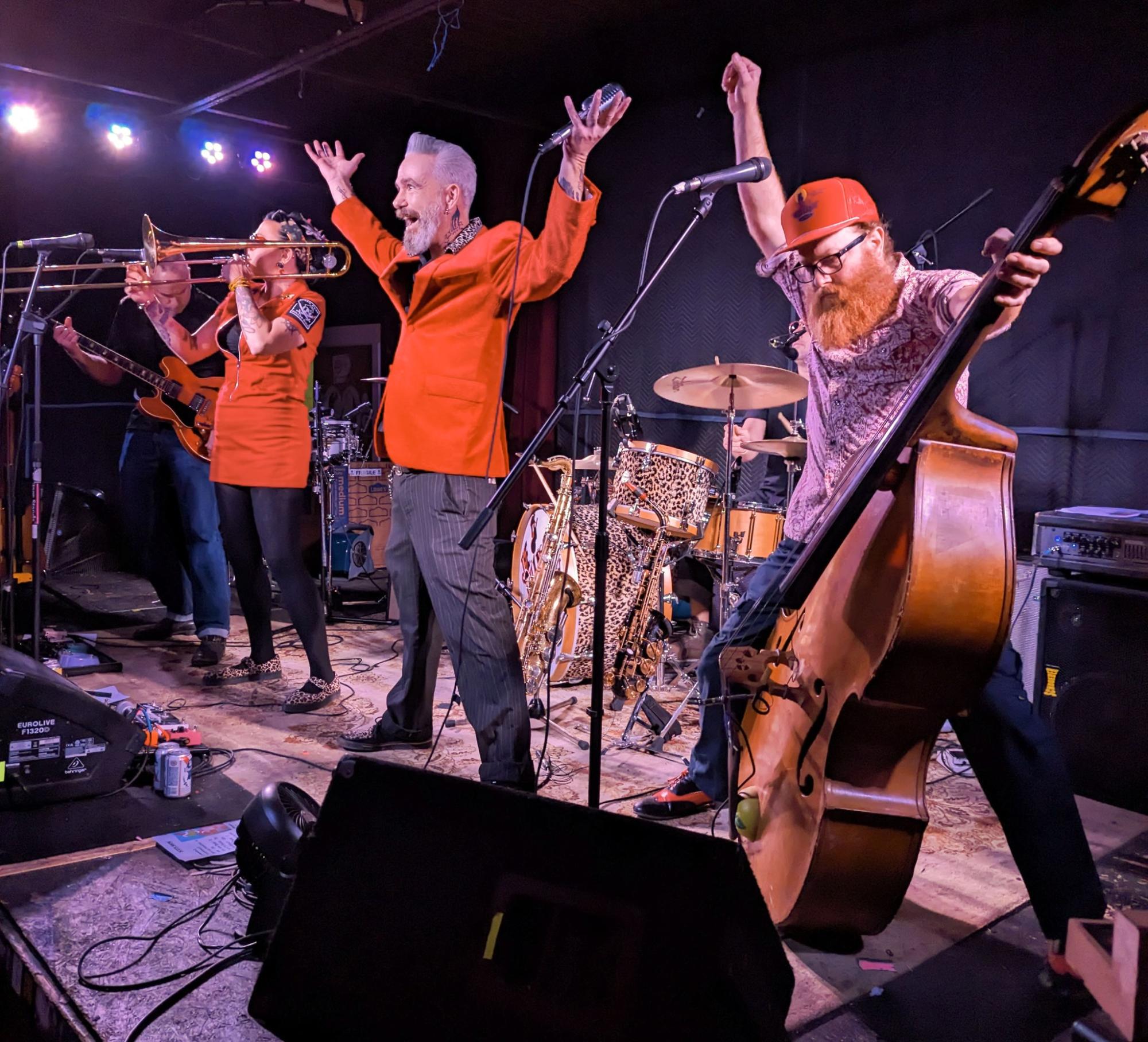Members of Phantom Playboys performing on stage in orange outfits