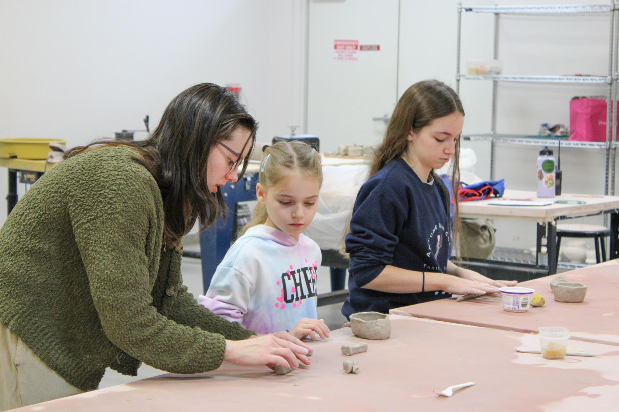 Two girls working with clay as their instructor helps them